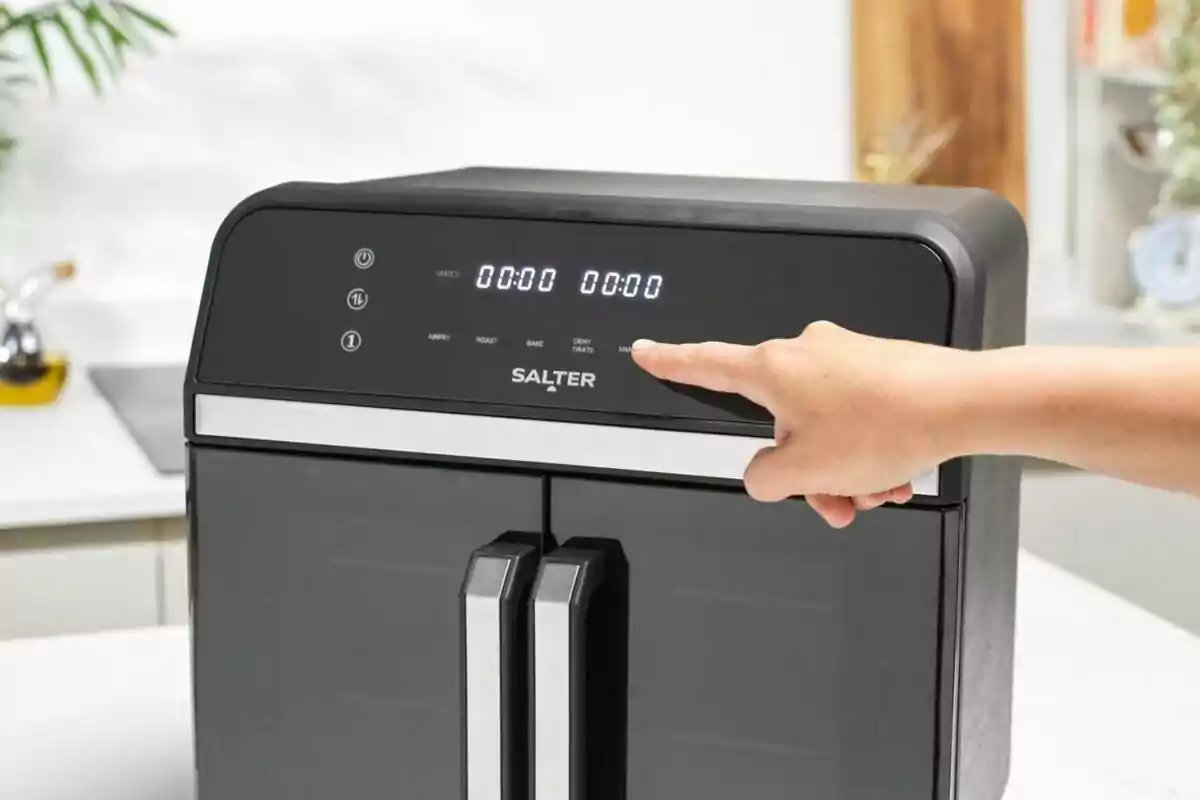 Persona utilitzant el panell digital d’una fregidora d’aire negra de la marca Salter en una cuina moderna