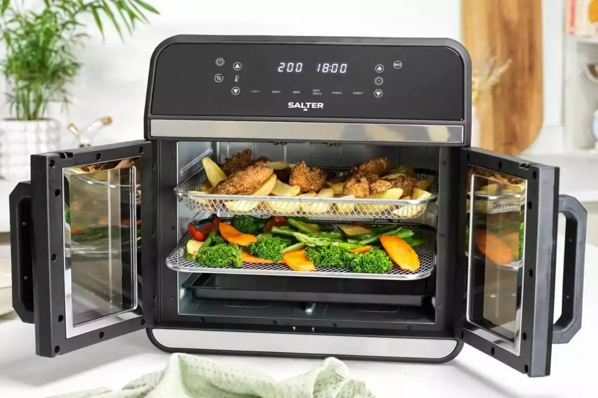 Fregidora d’aire de doble safata amb les portes obertes mostrant pollastre arrebossat, patates i verdures com bròquil, pastanagues i espàrrecs en una cuina moderna