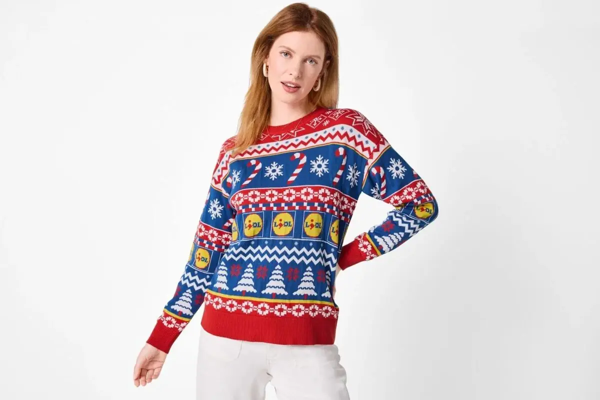 Dona amb jersei de Nadal colorit amb patrons de flocs de neu, bastons de caramel, arbres i logotips de Lidl, posant sobre fons blanc