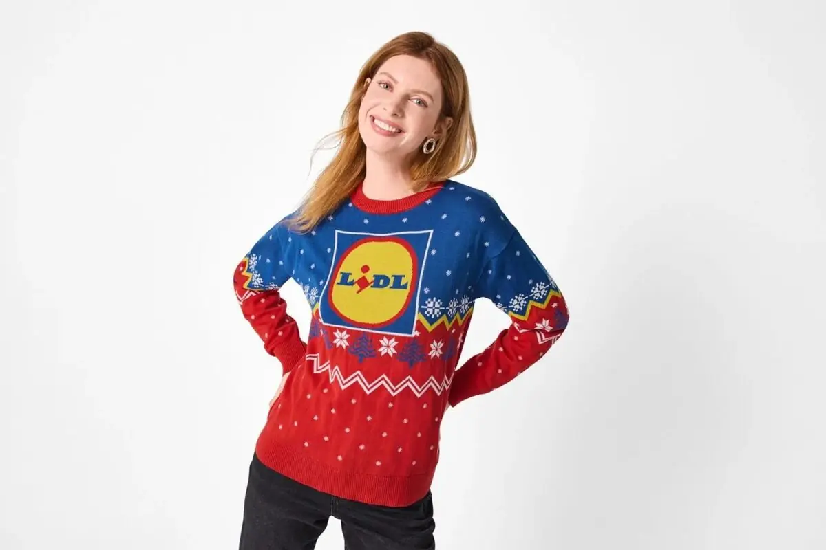 Dona somrient amb jersei de Nadal blau i vermell decorat amb el logotip de Lidl i flocs de neu