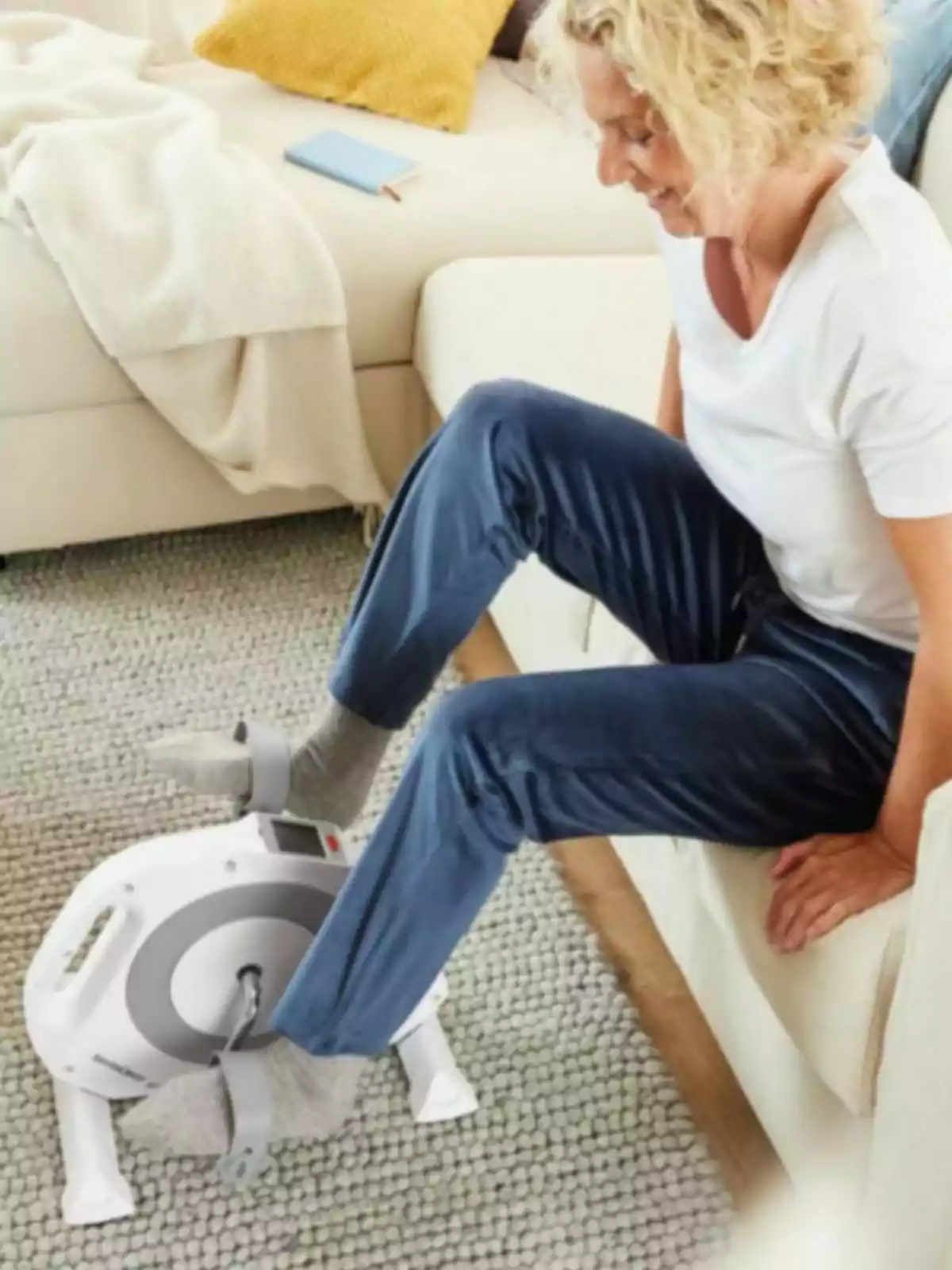 Dona asseguda en un sofà utilitzant una bicicleta estàtica petita per exercitar les cames en una sala acollidora