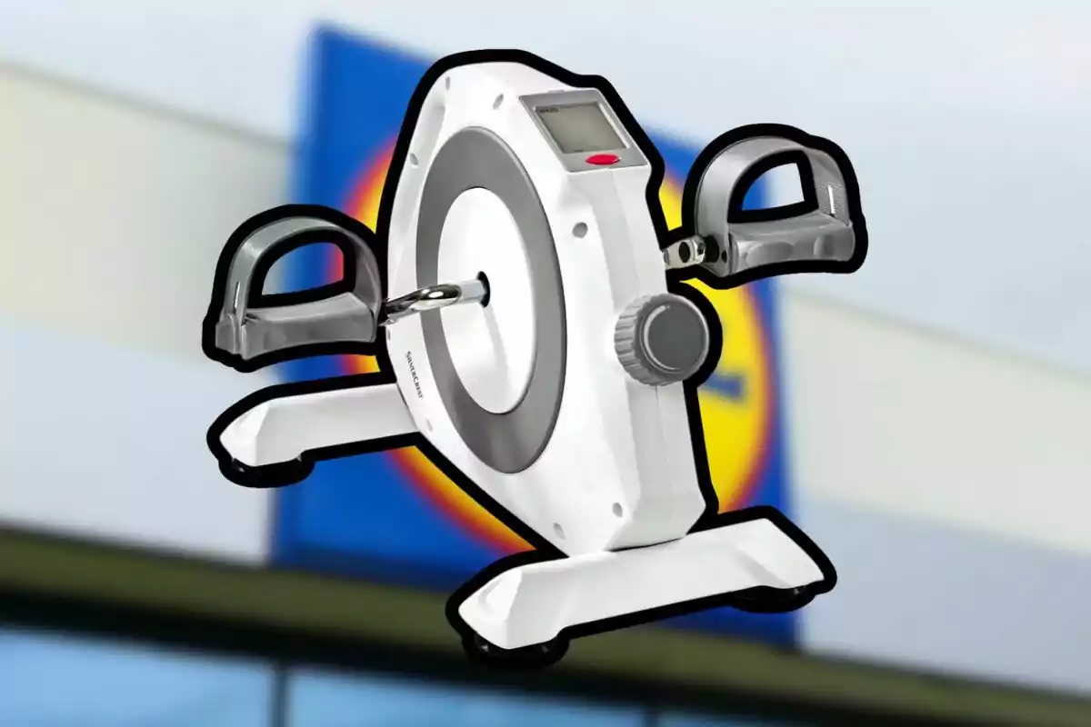 Bicicleta estàtica compacta de color blanc amb pedals i pantalla digital sobre un fons desenfocat d’una botiga.