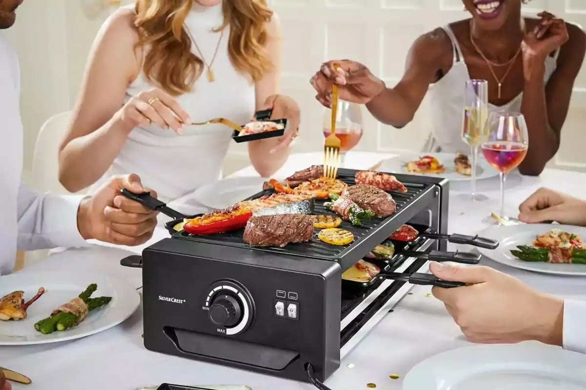 People sharing a meal around an electric grill with different types of meat and grilled vegetables in a cheerful atmosphere