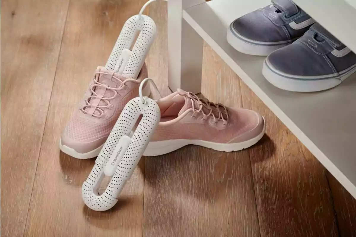 A pair of pink sneakers with electric deodorizing devices inside next to a shelf with gray athletic shoes on a wooden floor