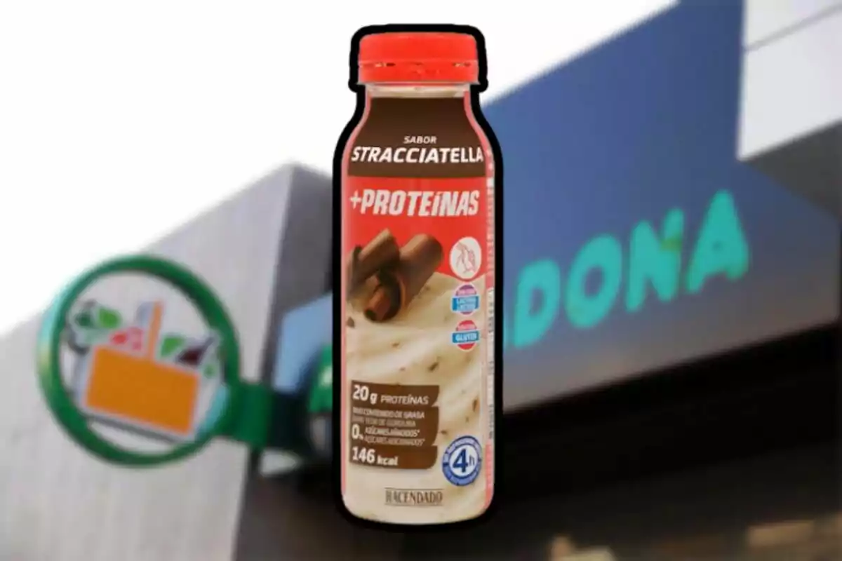 Botella de batido de proteínas sabor stracciatella de la marca Hacendado frente a la entrada de un supermercado Mercadona desenfocado.
