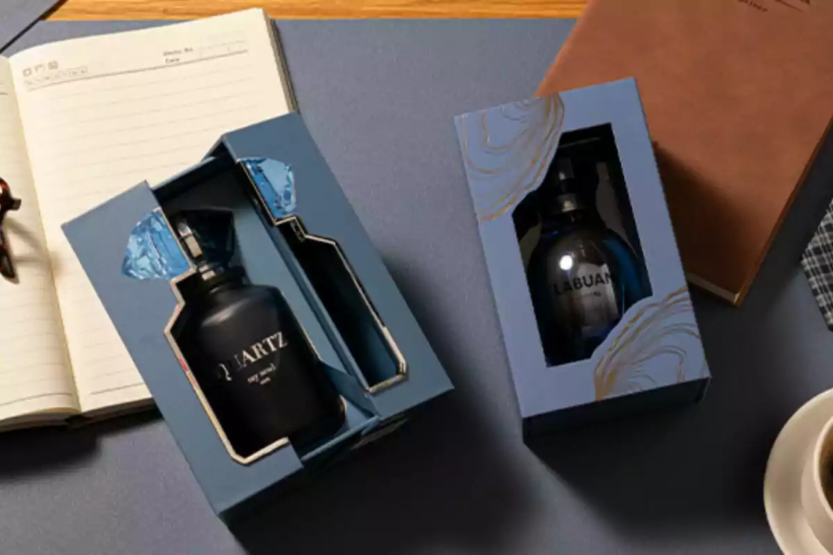 Dues capses de perfum de luxe sobre una taula al costat d’una llibreta, una tassa de cafè i una carpeta marró Dues capses de perfum de luxe sobre una taula al costat d’una llibreta, una tassa de cafè i una carpeta marró