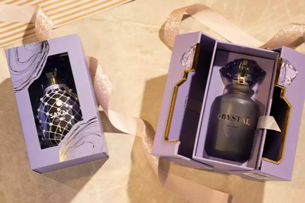 Dues caixes de perfum de color lila amb detalls daurats i tapes decoratives, una tancada i l’altra oberta mostrant el flascó a l’interior, sobre una superfície beix amb una cinta brillant. Dues caixes de perfum de color lila amb detalls daurats i tapes decoratives, una tancada i l’altra oberta mostrant el flascó a l’interior, sobre una superfície beix amb una cinta brillant.