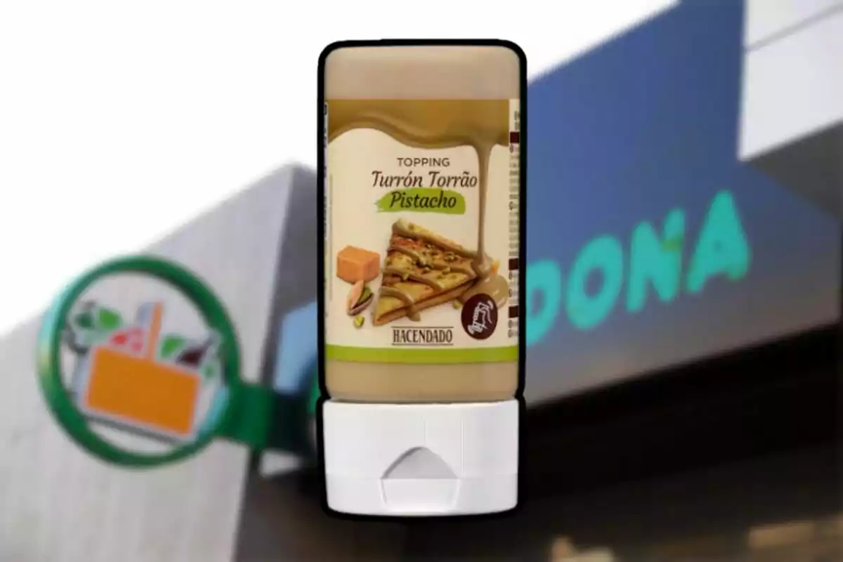 Envàs de topping de torró i festuc de la marca Hacendado davant d’una botiga Mercadona desenfocada Envàs de topping de torró i festuc de la marca Hacendado davant d’una botiga Mercadona desenfocada