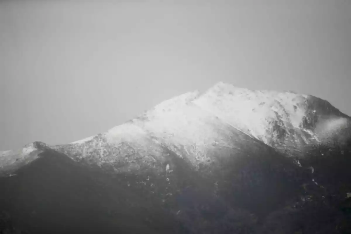 Cima de una montaña cubierta parcialmente de nieve bajo un cielo nublado.