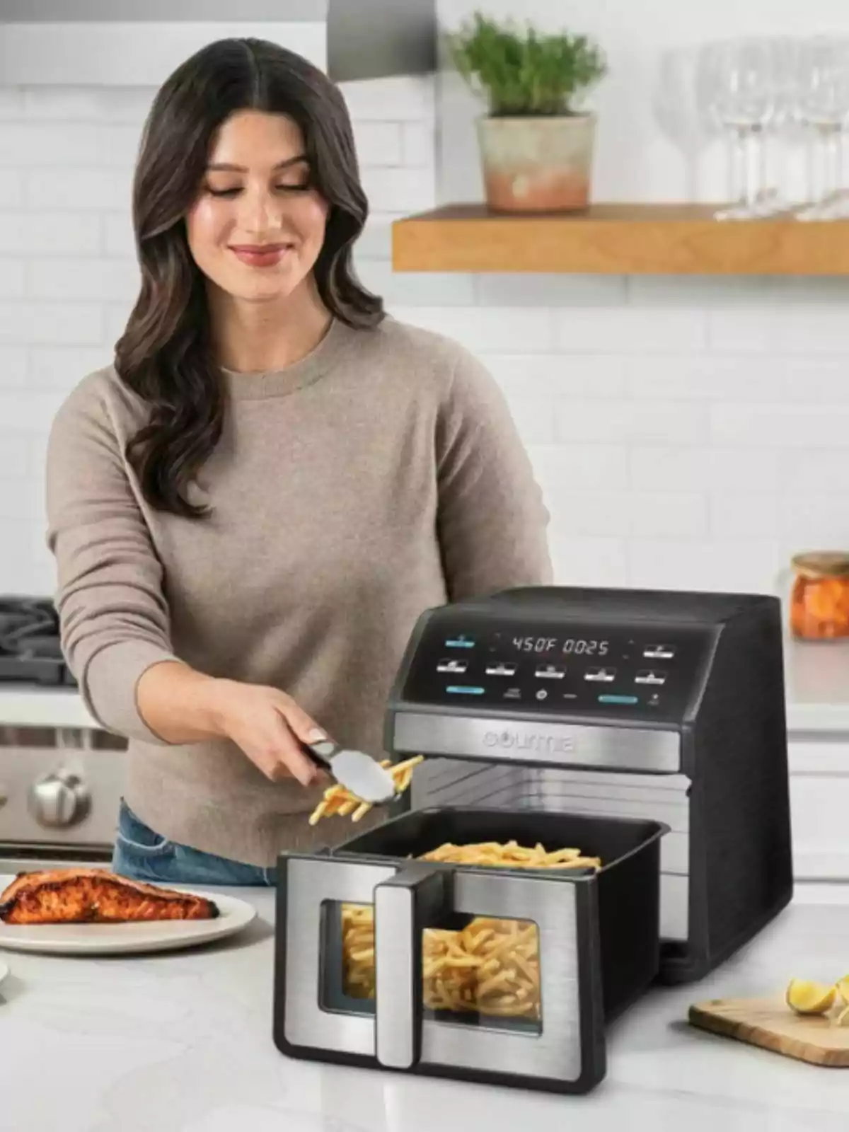 Woman smiling while serving French fries from a Costco air fryer in a modern kitchen.