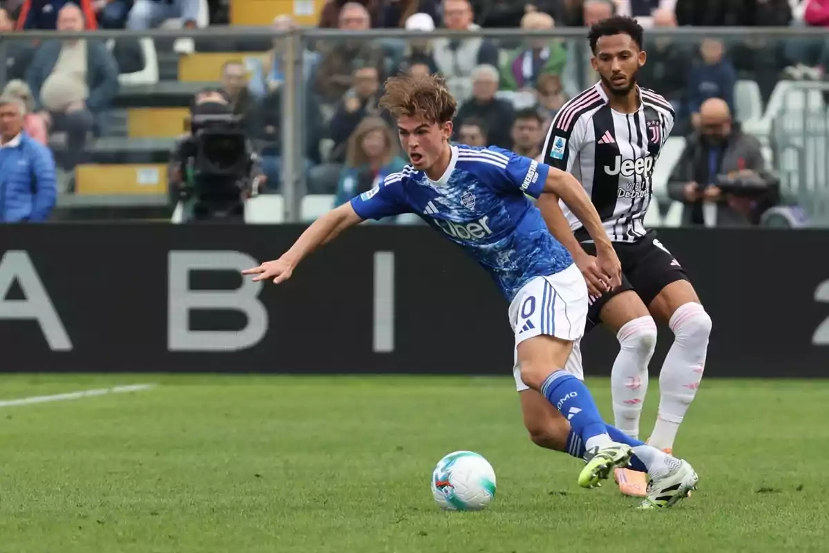 Dos futbolistes disputen la pilota durant un partit en un estadi ple d’espectadors