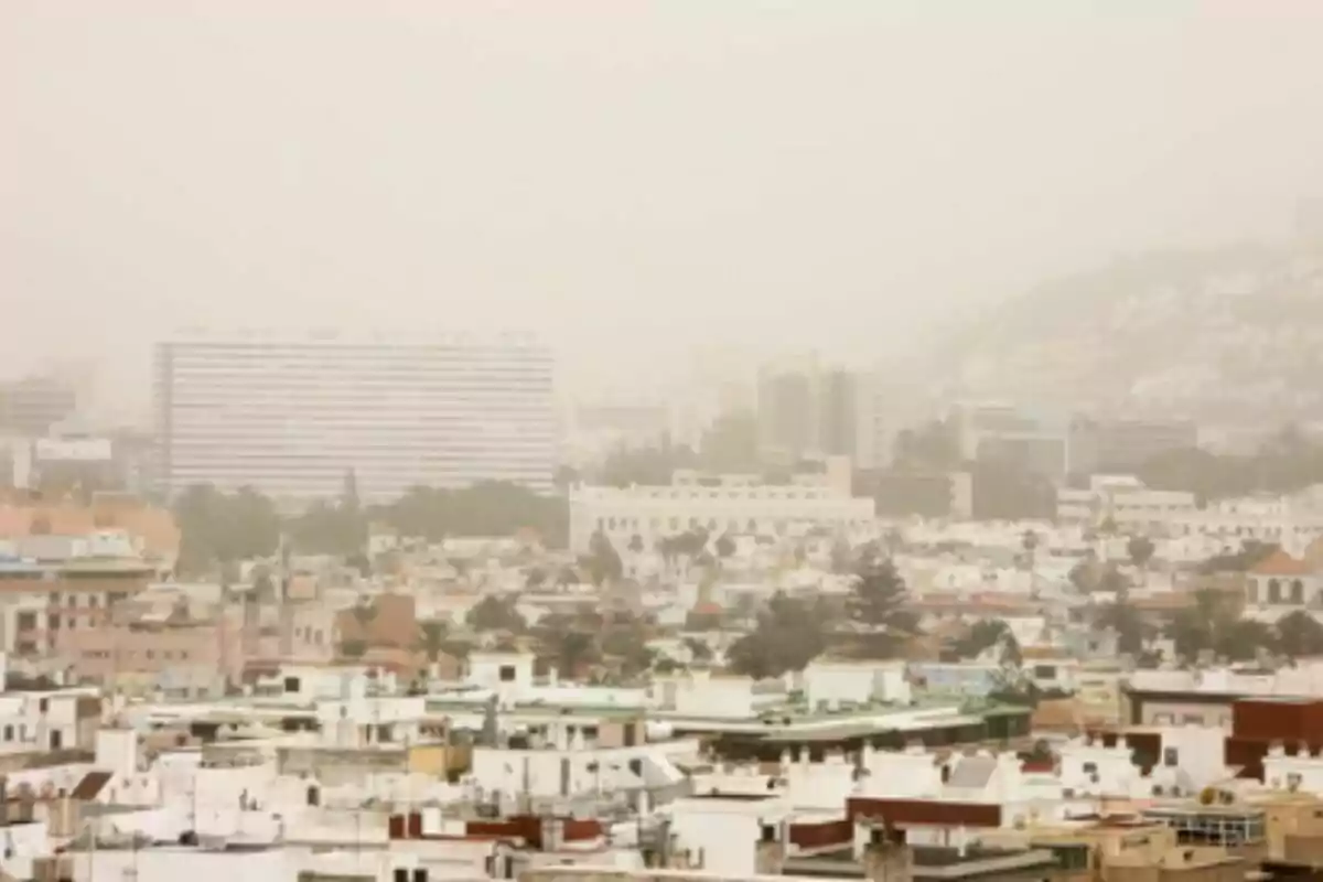 Vista de una ciudad con edificios y casas bajo una densa capa de polvo o neblina que reduce la visibilidad. Vista de una ciudad con edificios y casas bajo una densa capa de polvo o neblina que reduce la visibilidad.