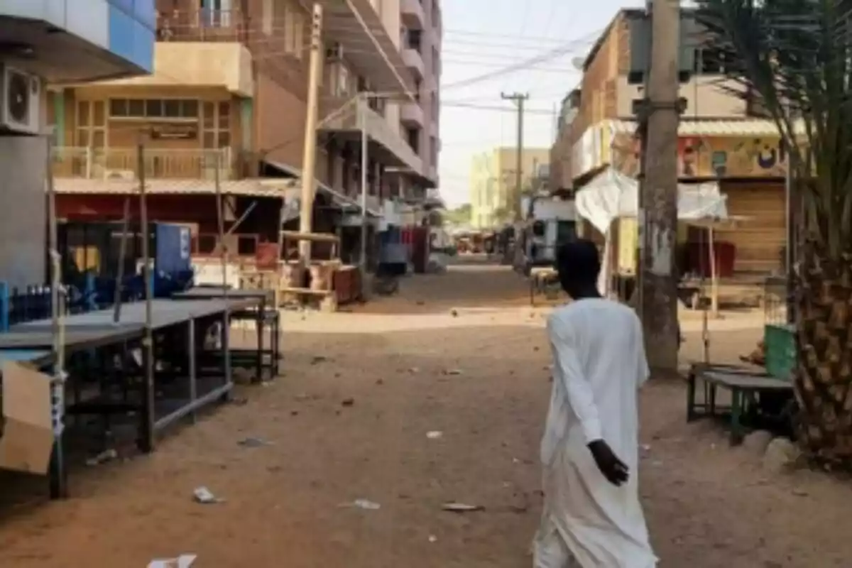 Hombre de espaldas caminando por una calle vacía con puestos cerrados y edificios a los lados en Sudán. Hombre de espaldas caminando por una calle vacía con puestos cerrados y edificios a los lados en Sudán.