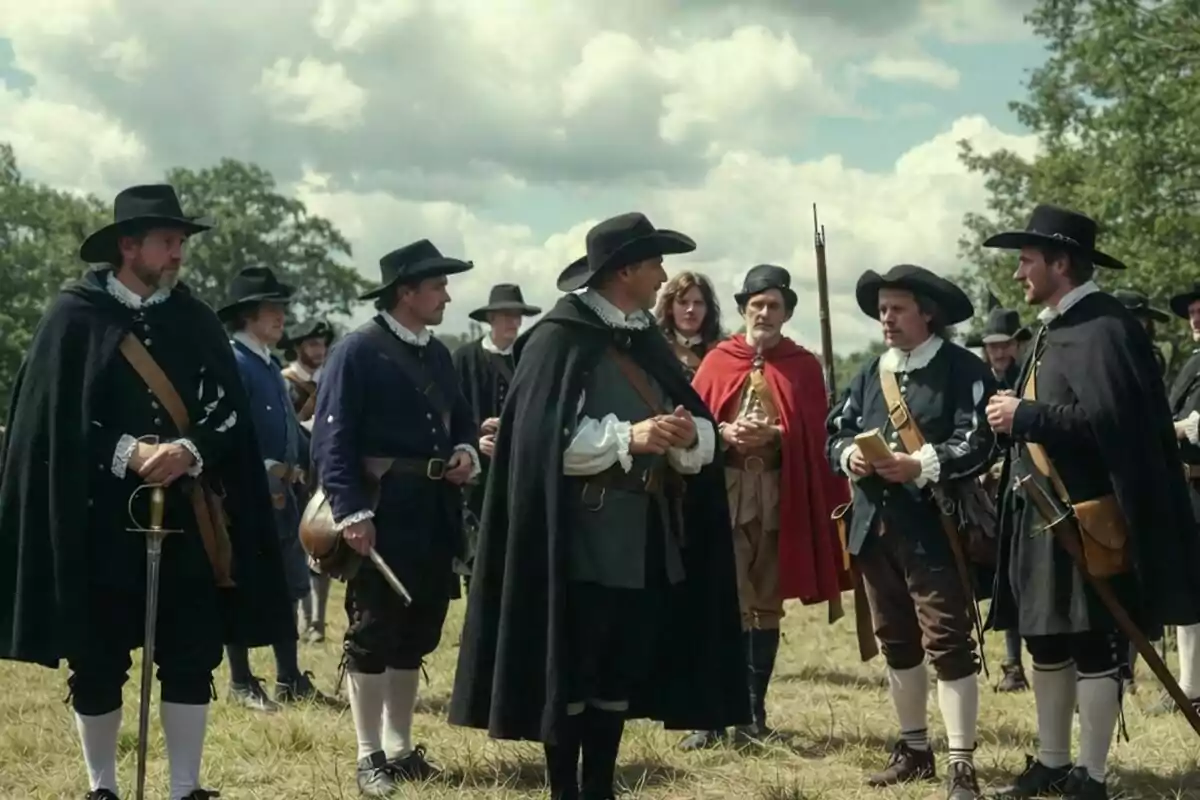 Grup d’homes vestits amb vestits històrics i barrets d’ala ampla conversant a l’aire lliure en un camp sota un cel ennuvolat. Grup d’homes vestits amb vestits històrics i barrets d’ala ampla conversant a l’aire lliure en un camp sota un cel ennuvolat.