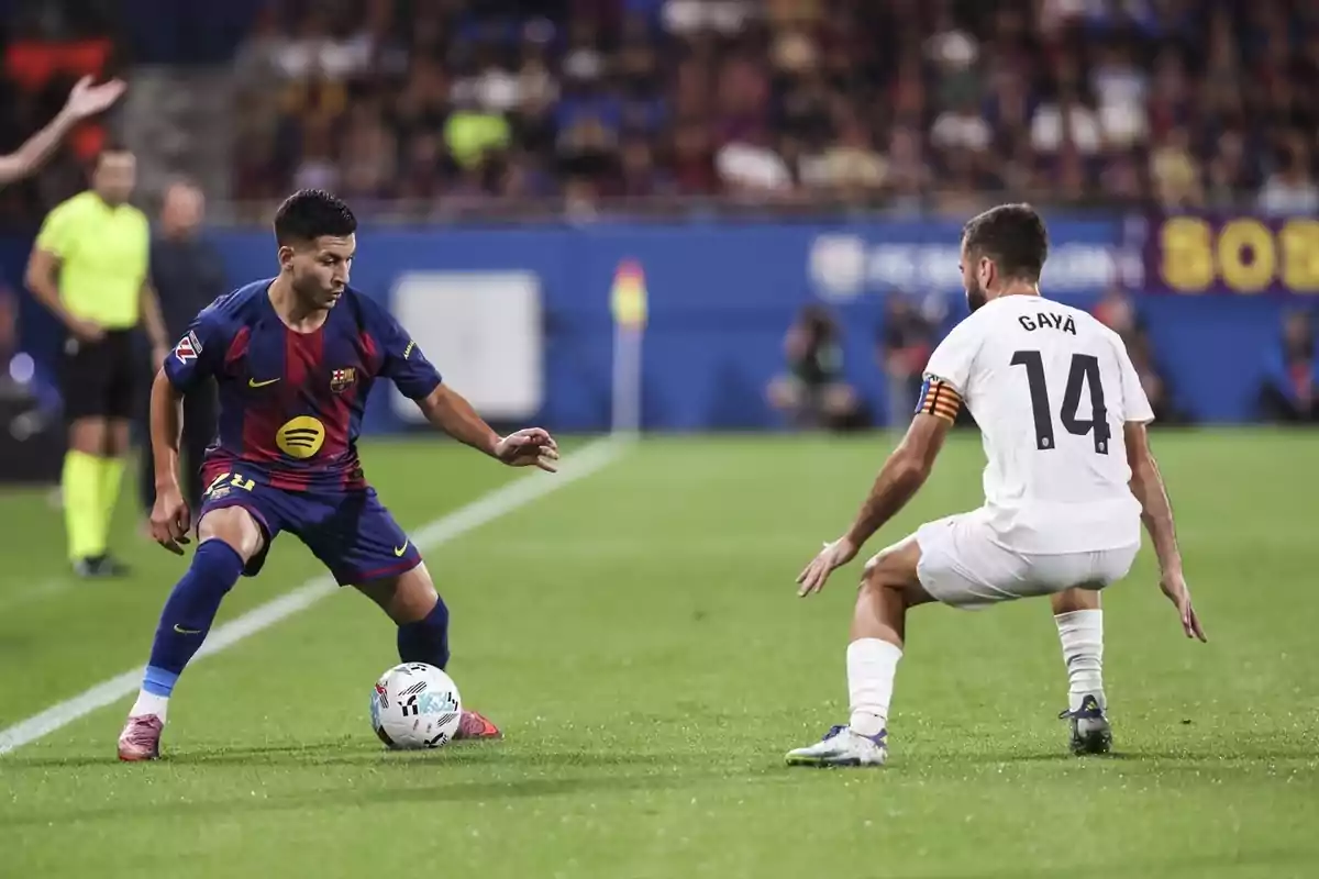 Two players compete for the ball during a match between Barcelona and Valencia in a stadium full of spectators.