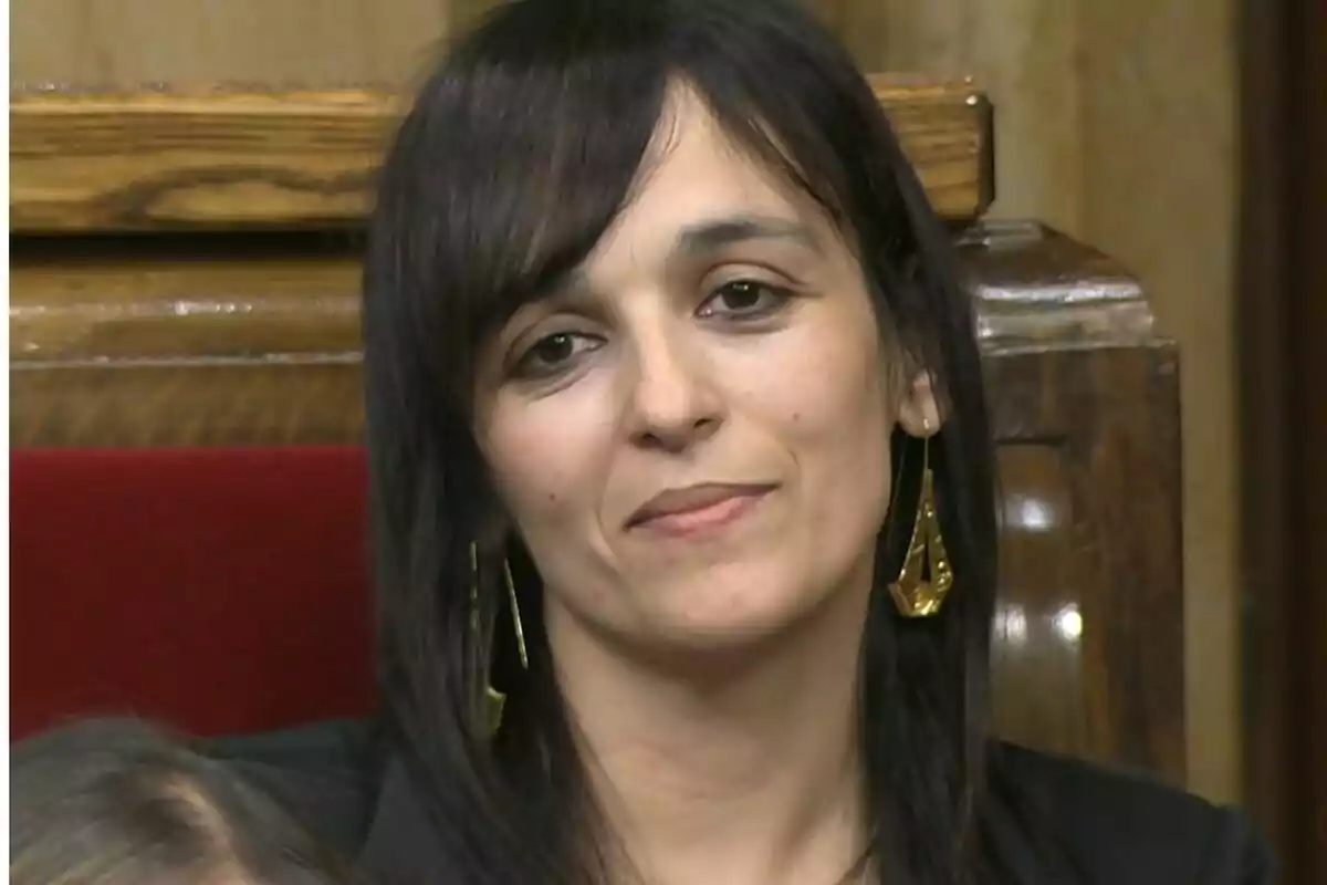 Dona de cabell fosc i llis amb arracades daurades asseguda en un banc de fusta