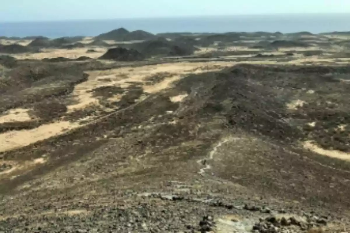 Paisatge àrid amb turons de terra fosca i el mar al fons sota un cel serè a Canàries.
