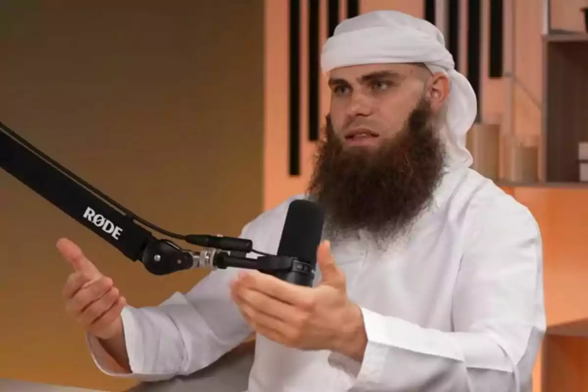 Home amb barba i vestimenta tradicional blanca parlant davant d’un micròfon durant una gravació a l’estudi