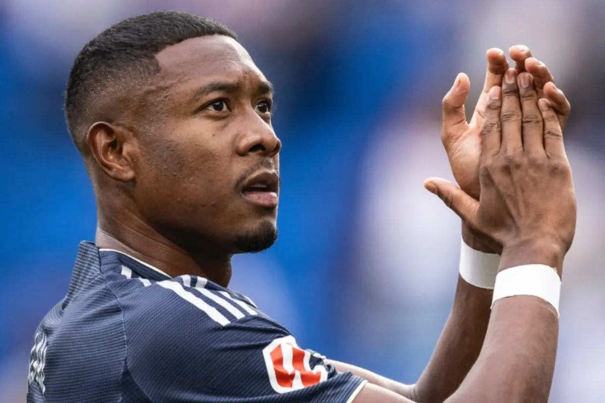 Futbolista aplaudint al camp amb expressió seriosa i fons desenfocat blau