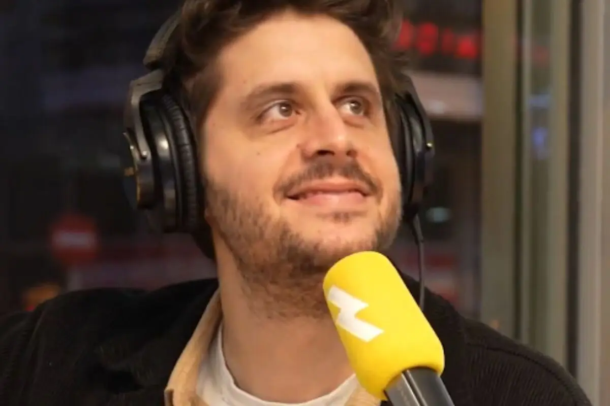Hombre con auriculares grandes hablando sonriente frente a un micrófono amarillo en un estudio de radio