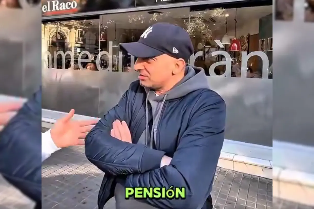 Hombre con gorra y chaqueta azul cruzado de brazos en la calle frente a un local con la palabra PENSIÓN en letras verdes en la parte inferior de la imagen