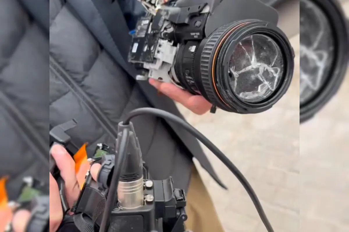 Persona sosteniendo una cámara profesional con el lente roto y partes internas expuestas