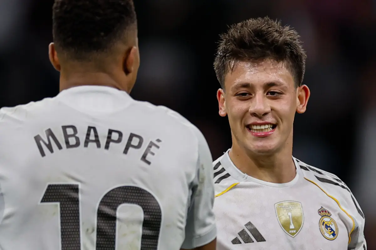 Two Real Madrid players smile and talk on the field during a match, one of them wearing a jersey with the name Mbappé and the number 10.