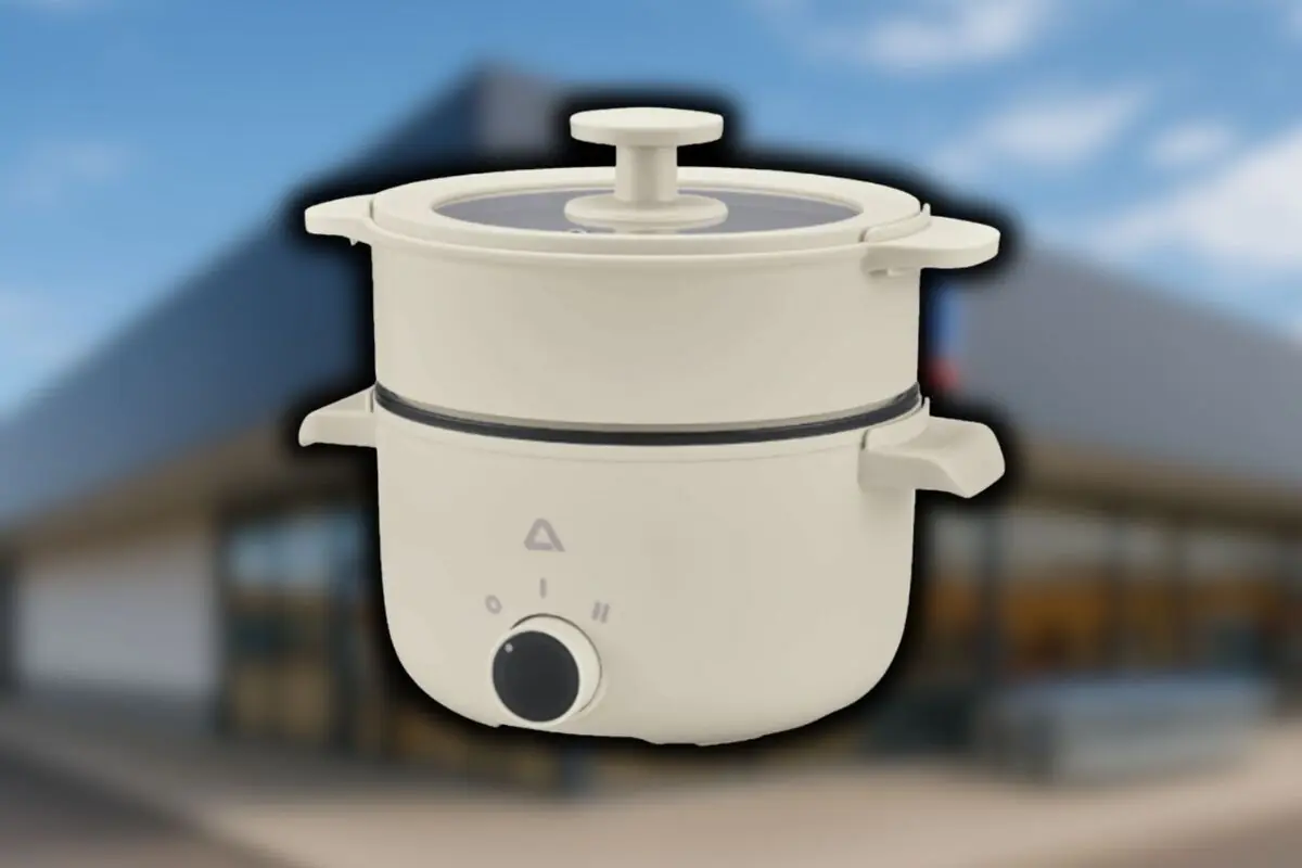 Arrocera eléctrica multifunción de color crema de Aldi con tapa de cristal y mando giratorio sobre fondo de una tienda de la mencionada cadena desenfocada.