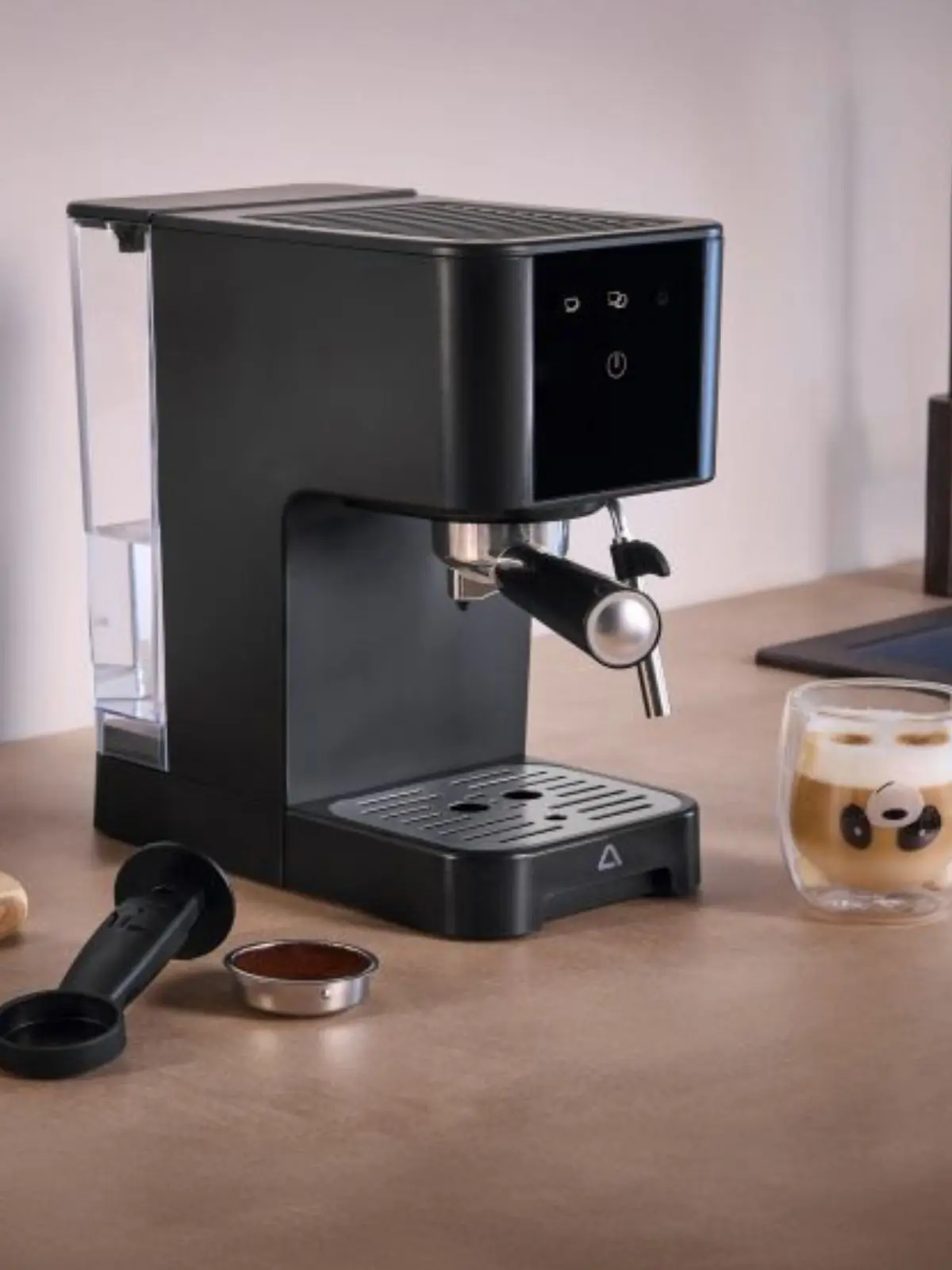Cafetera espresso negra moderna de Aldi sobre una encimera con accesorios y una taza de café con espuma.