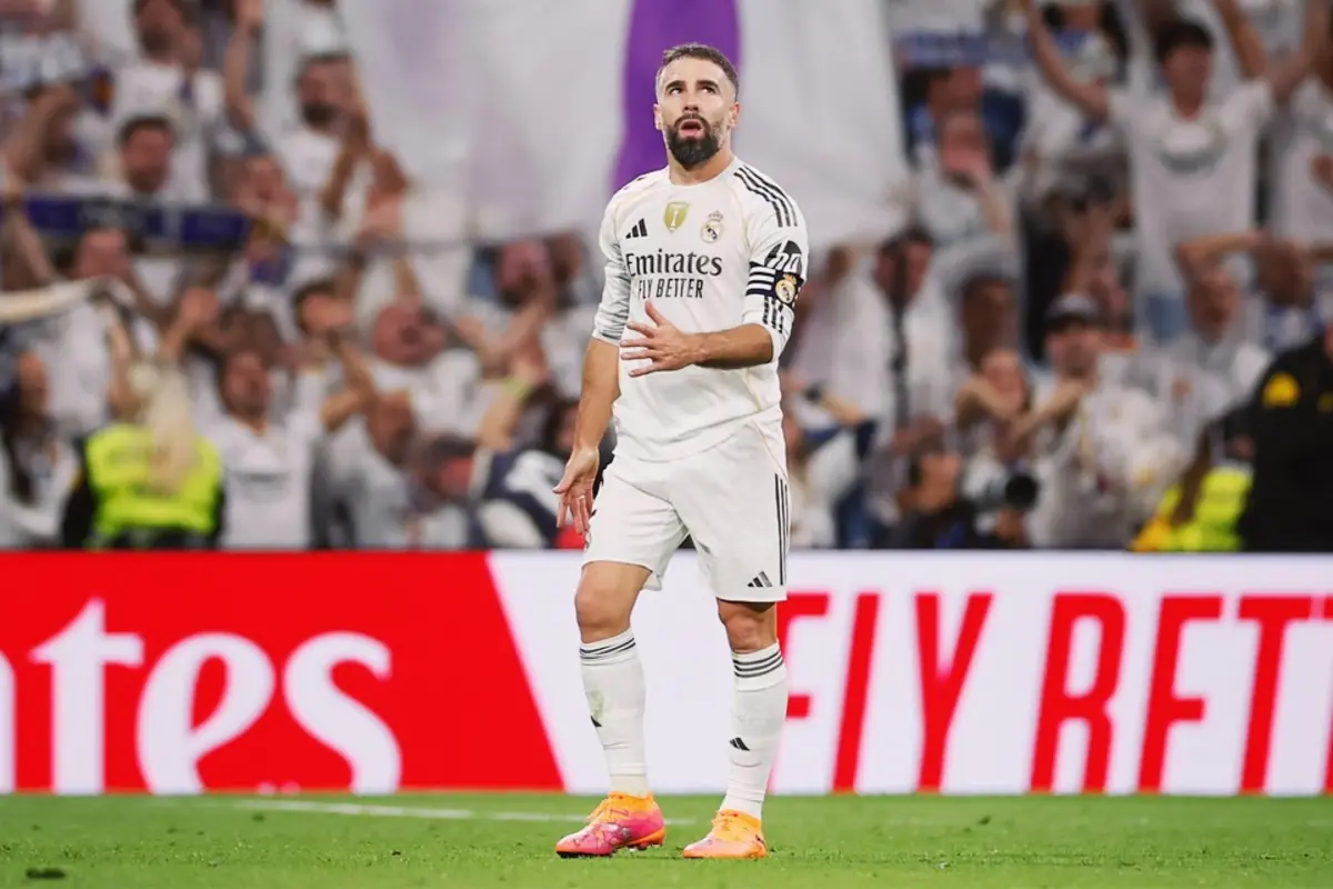 Real Madrid player on the field wearing a white uniform and captain's armband during a match with fans in the background