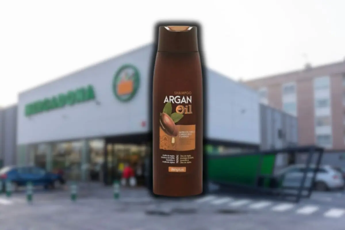 Botella de champú de aceite de argán Deliplus en primer plano con un supermercado Mercadona desenfocado al fondo