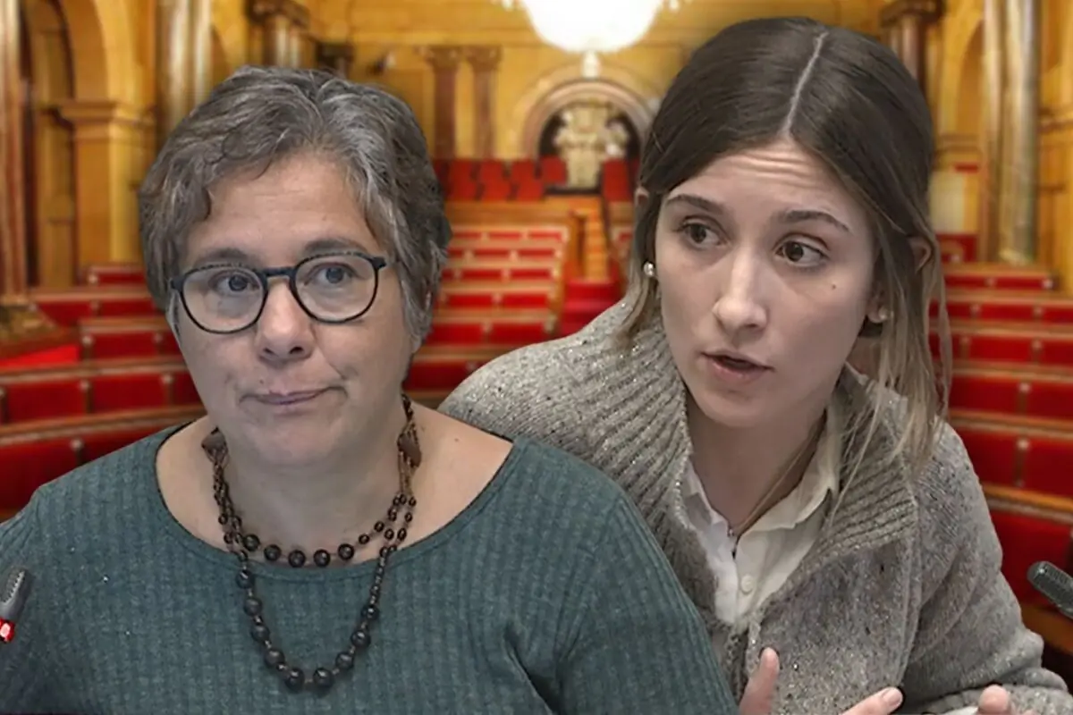 Dos mujeres conversan en un hemiciclo parlamentario con escaños rojos de fondo