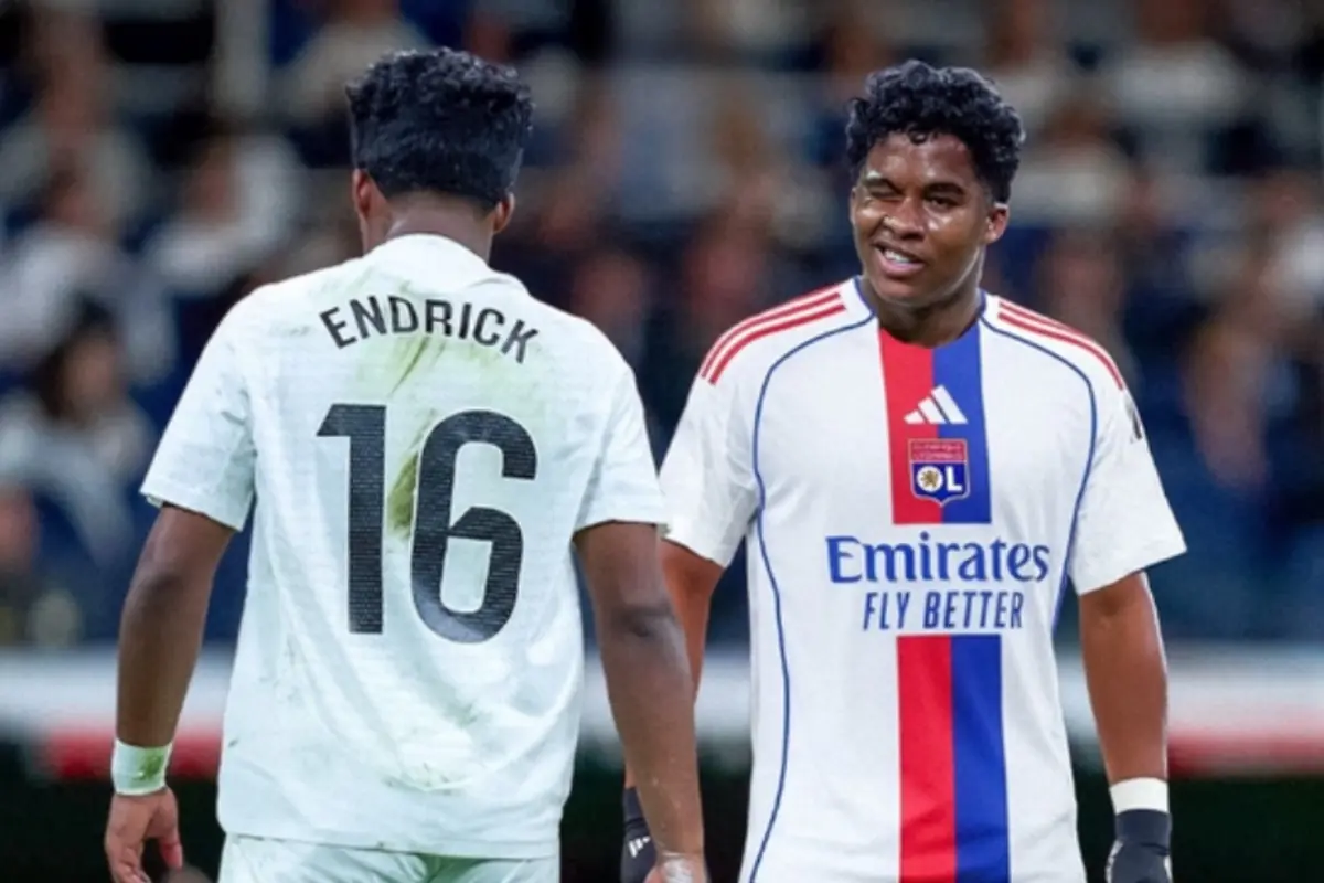 Dos futbolistes joves conversen al camp durant un partit, un amb samarreta blanca i dorsal 16 amb el nom Endrick i l’altre amb uniforme blanc de l’Olympique de Lió amb franja blava i vermella i patrocini Emirates Fly Better