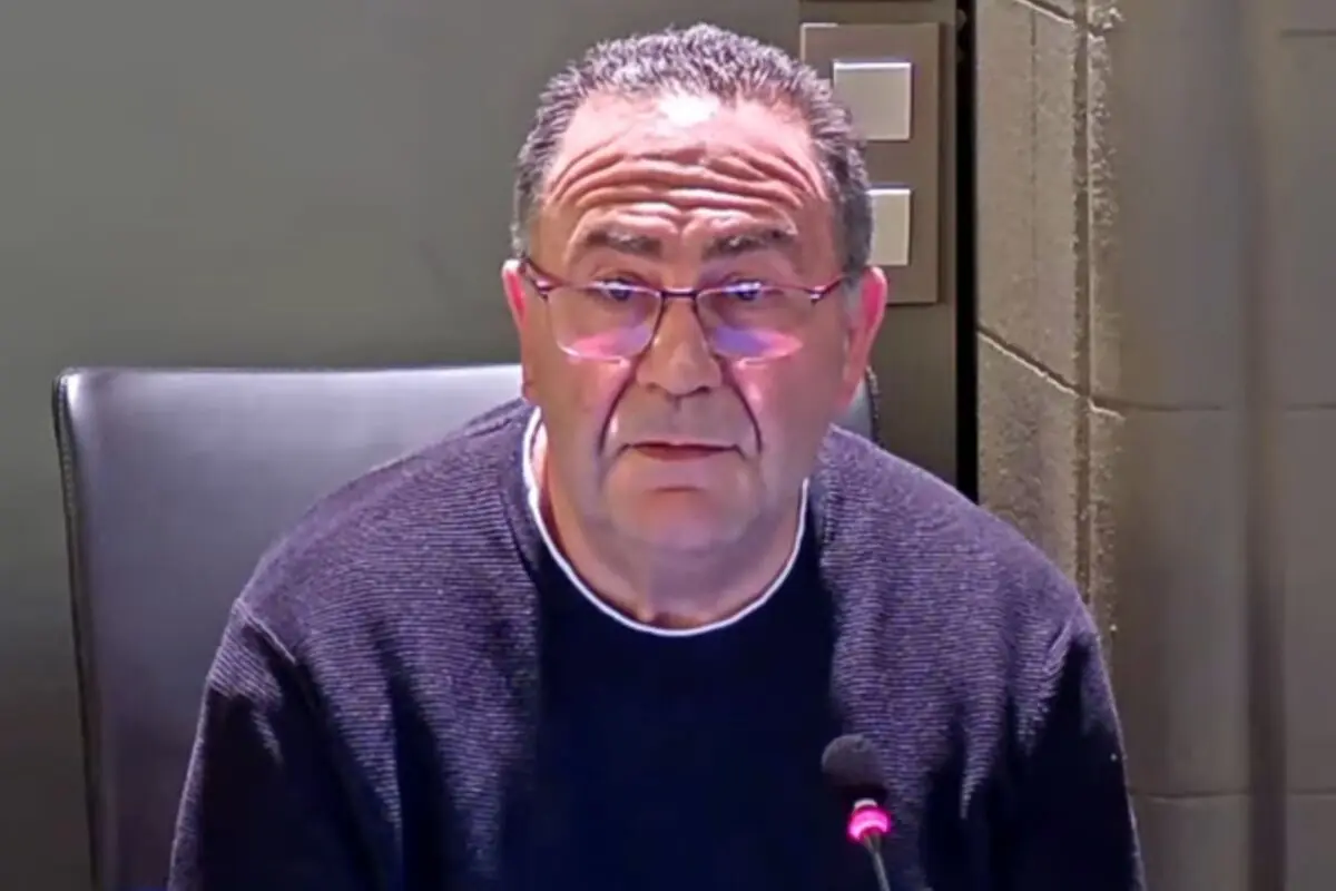 Hombre de mediana edad con gafas y suéter oscuro sentado frente a un micrófono en una sala iluminada