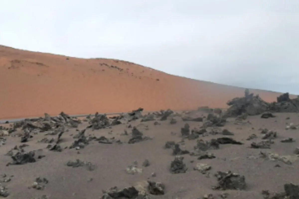 Paisatge desèrtic de Lanzarote amb dunes de sorra ataronjada i roques fosques disperses sota un cel ennuvolat.