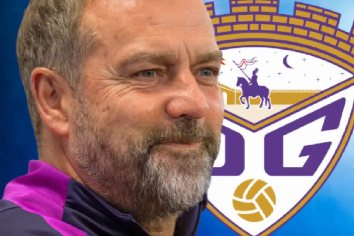 Home de barba i cabells canosos amb jaqueta esportiva davant d’un escut d’equip de futbol amb colors morat i daurat