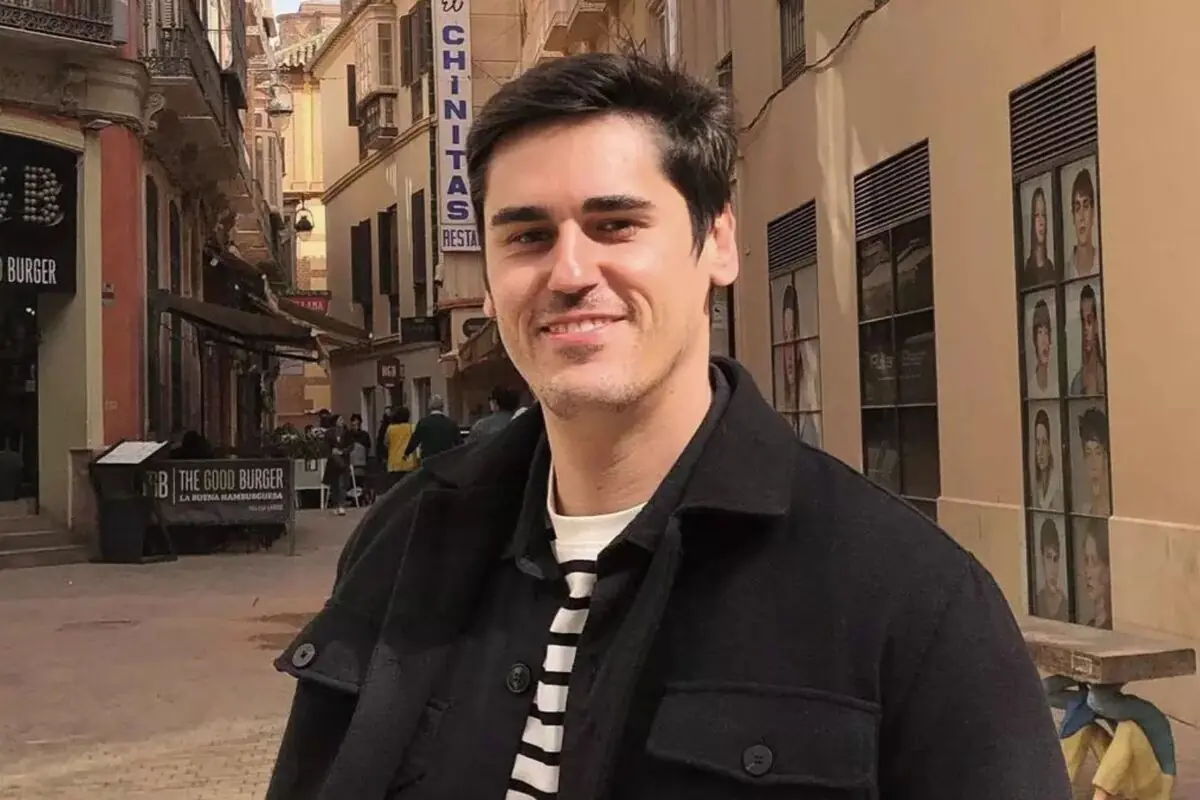 Home jove somrient en un carrer de vianants amb edificis i rètols al fons