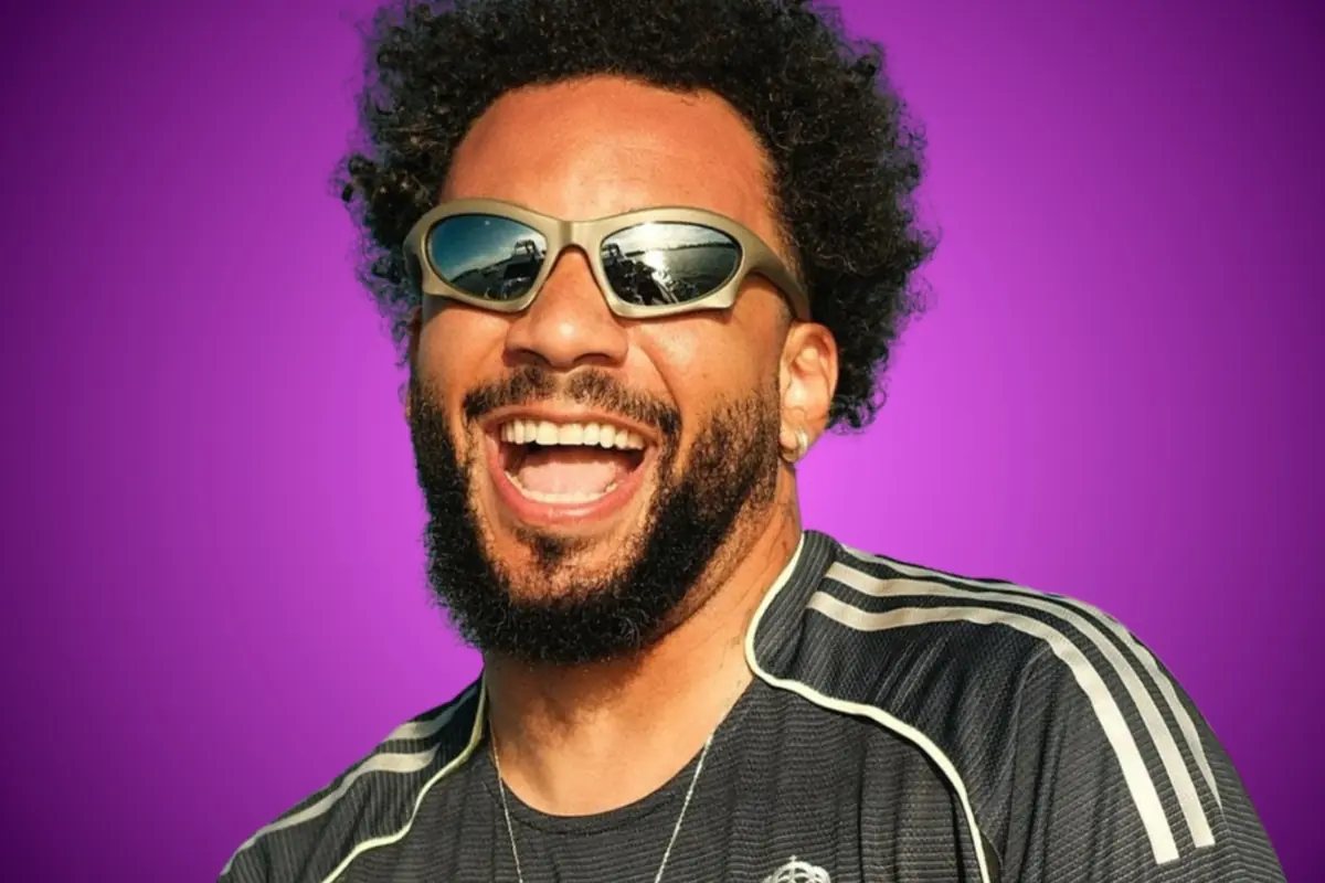 Home amb ulleres de sol esportives somrient i vestint una samarreta negra amb ratlles blanques sobre un fons morat