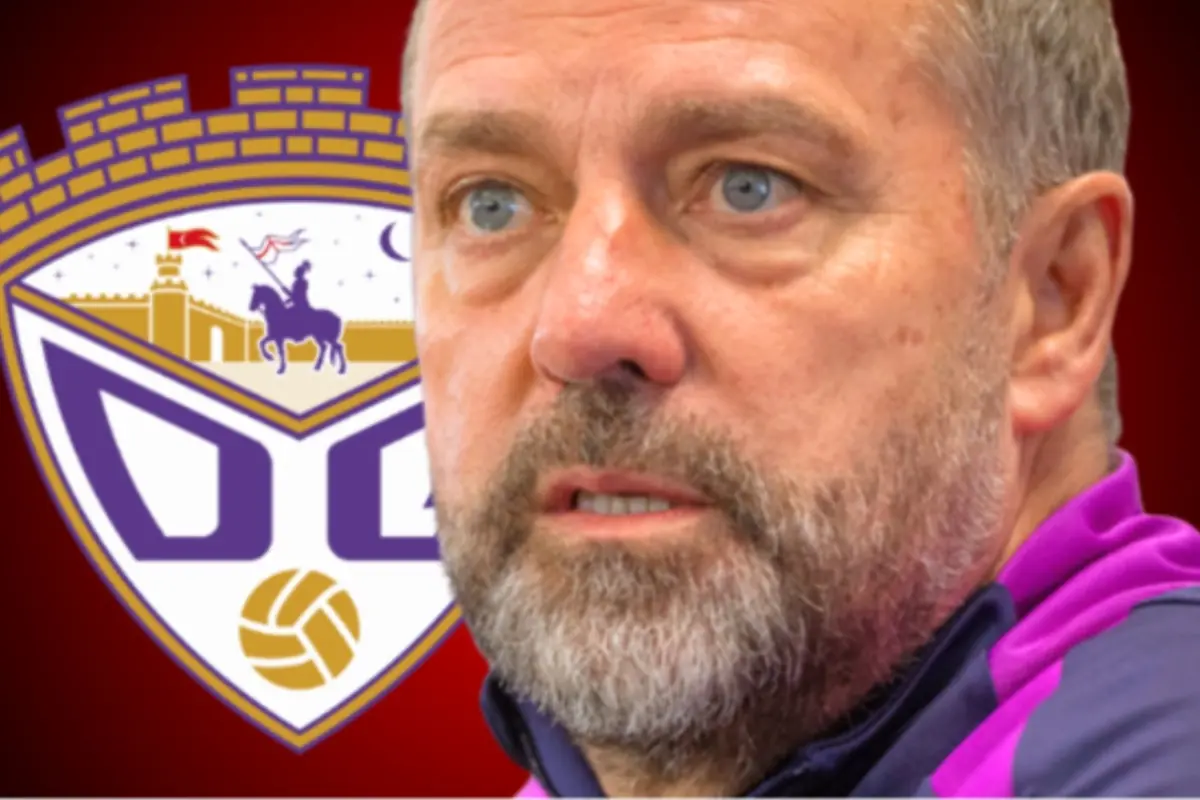 Primer pla d’un entrenador de futbol de mitjana edat amb barba davant de l’escut morat i daurat d’un club esportiu