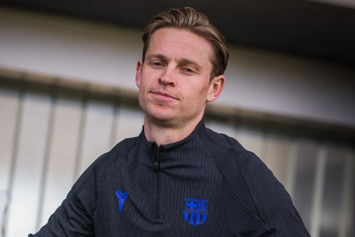 Persona amb jaqueta esportiva negra del FC Barcelona posant davant d’una estructura metàl·lica desenfocada