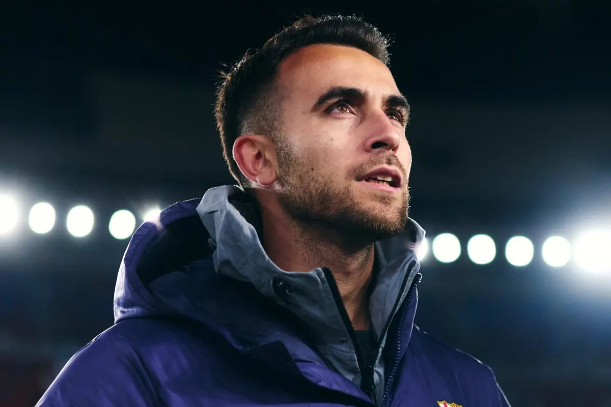 Hombre joven con chaqueta deportiva mirando hacia arriba en un estadio iluminado por focos de fondo
