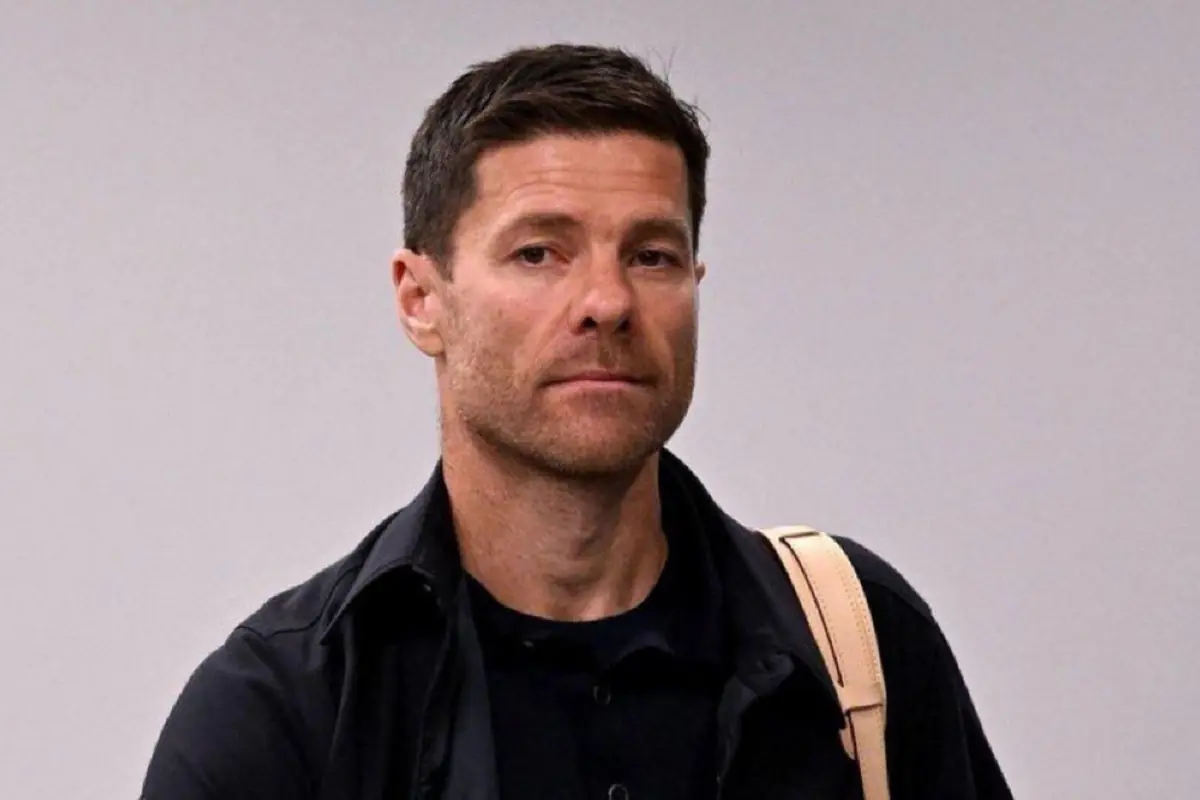 Short-haired man with a light beard wearing dark clothes and a light-colored backpack over his shoulder, looking ahead with a serious expression