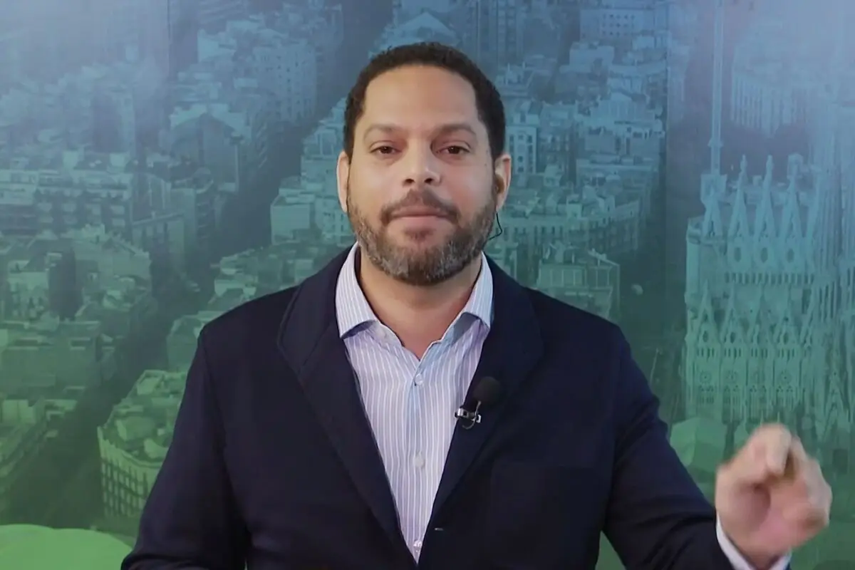 Home amb barba i jaqueta fosca parlant davant d’un fons de ciutat