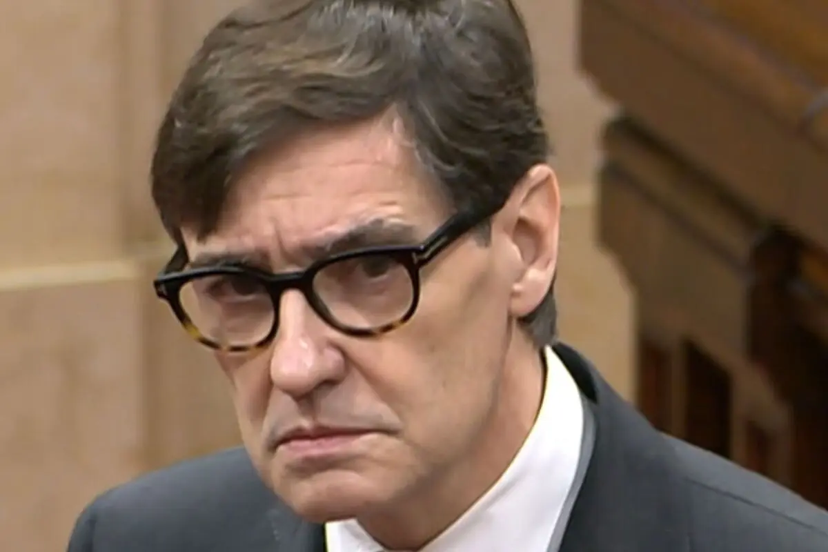 Primer pla d’un home amb ulleres de pasta fosca, gest seriós i vestit formal en un entorn institucional