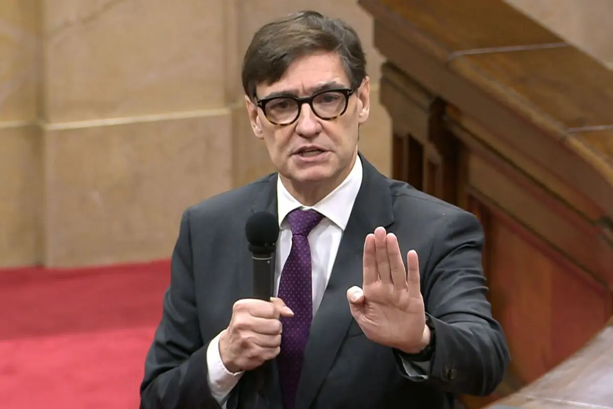 Hombre con gafas y traje oscuro hablando con un micrófono en la mano y gesto de detener con la otra mano en un salón parlamentario