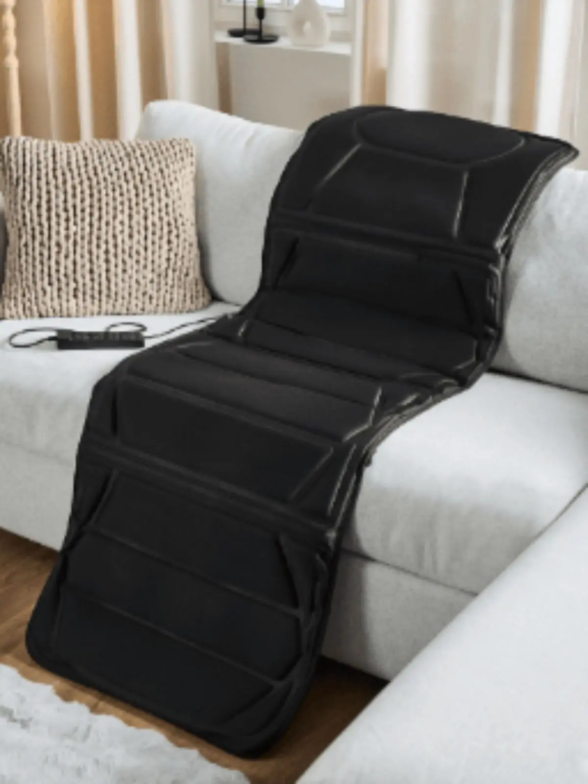 Colchón masajeador negro de Aldi extendido sobre un sofá claro en una sala de estar.