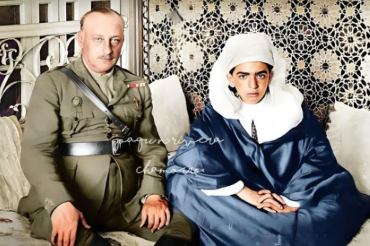 Primo de Rivera con uniforme militar y una persona vestida con ropa tradicional marroquí están sentados juntos en un sofá decorado con un fondo de mosaicos.