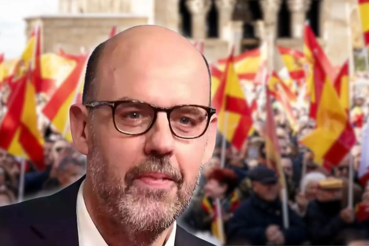 Hombre con gafas y barba en primer plano con una multitud al fondo ondeando banderas de España