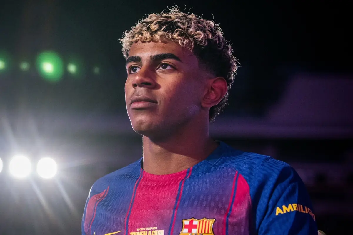 Jove futbolista amb cabell arrissat i tenyit de ros portant l’uniforme blau i grana del FC Barcelona sota llums brillants