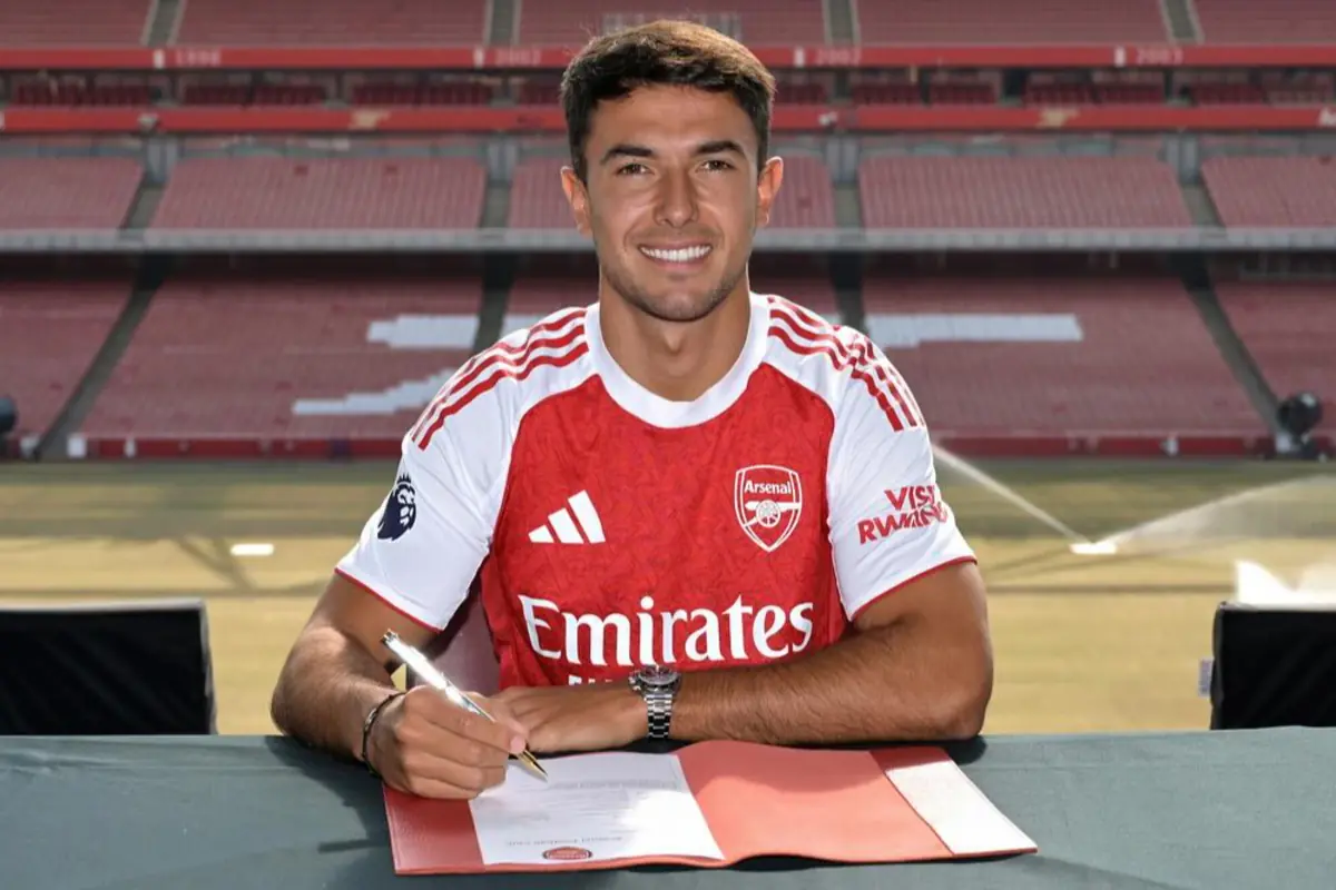 Futbolista amb samarreta de l’Arsenal signant un contracte en un estadi buit